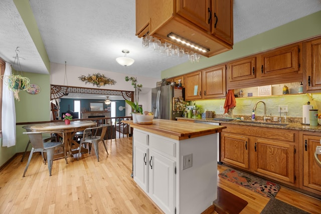 kitchen featuring a sink, light wood-style floors, stainless steel fridge, a textured ceiling, and butcher block counters