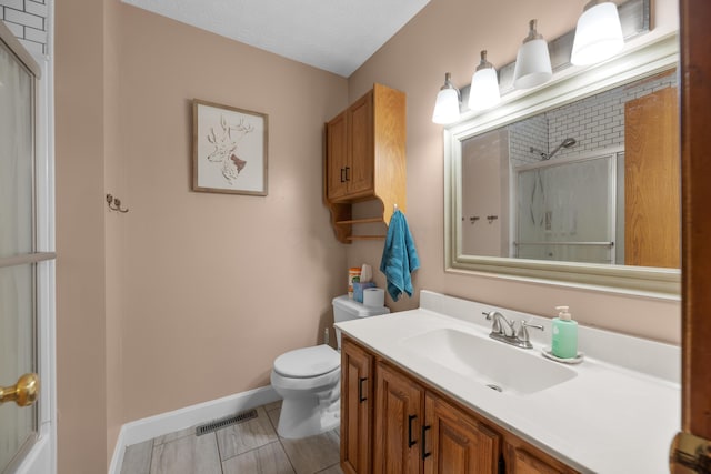 bathroom with vanity, toilet, visible vents, baseboards, and a shower with door