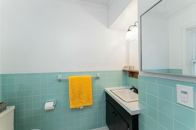 bathroom with crown molding, vanity, a wainscoted wall, and tile walls