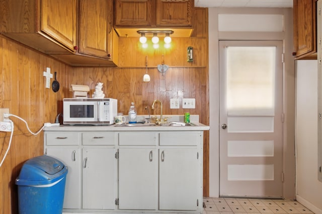 kitchen featuring white microwave, light countertops, white cabinetry, wood walls, and a sink