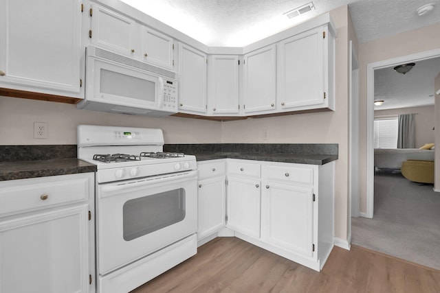 kitchen with dark countertops, white appliances, light wood-type flooring, white cabinets, and visible vents