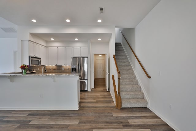 8050 Flint Run Pl, Columbus, OH 43235 - kitchen with stainless steel appliances, a peninsula, a breakfast bar, light stone counters, and dark wood-type flooring