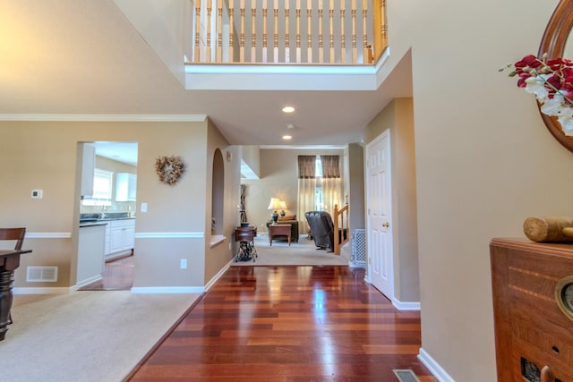 foyer entrance with crown molding, wood finished floors, arched walkways, baseboards, and visible vents
