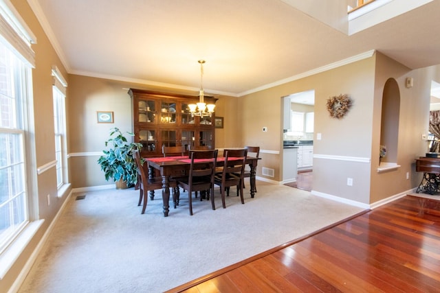 dining room featuring arched walkways, visible vents, an inviting chandelier, wood finished floors, and crown molding