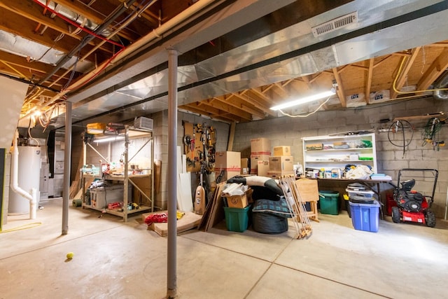 unfinished basement featuring concrete block wall, a workshop area, visible vents, and gas water heater