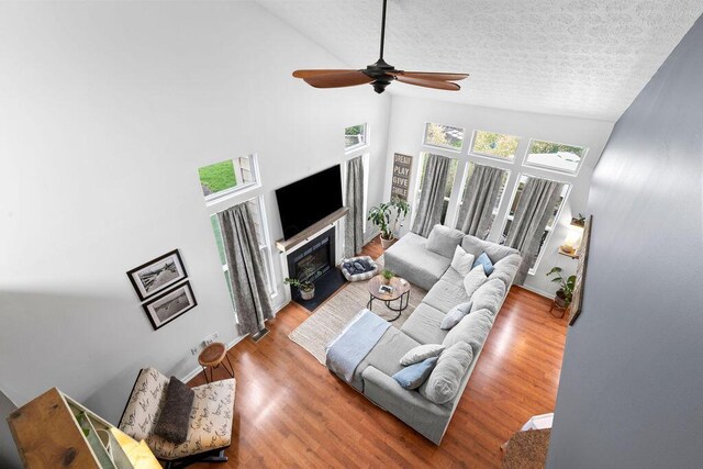 3379 Fishinger Mill Dr, Hilliard, OH 43026 - living area with high vaulted ceiling, a glass covered fireplace, a ceiling fan, wood finished floors, and a textured ceiling