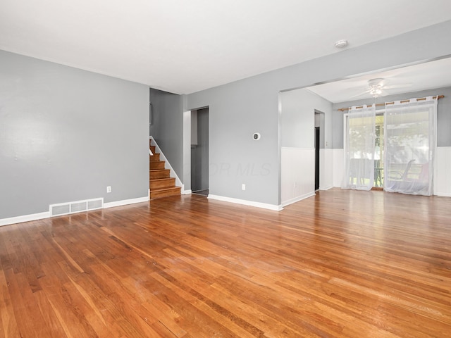 empty room with light wood finished floors, stairway, ceiling fan, and baseboards