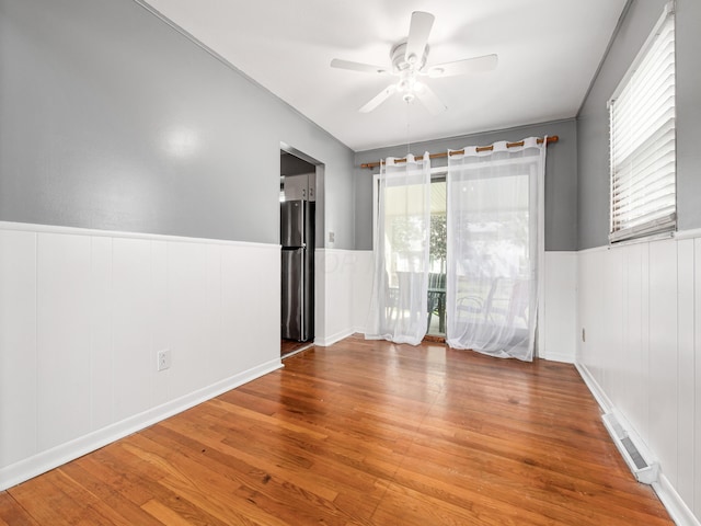 unfurnished room featuring a wainscoted wall, wood finished floors, a ceiling fan, and a decorative wall