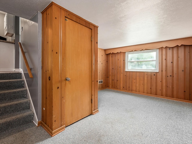 unfurnished bedroom featuring carpet flooring, a textured ceiling, baseboards, and wooden walls