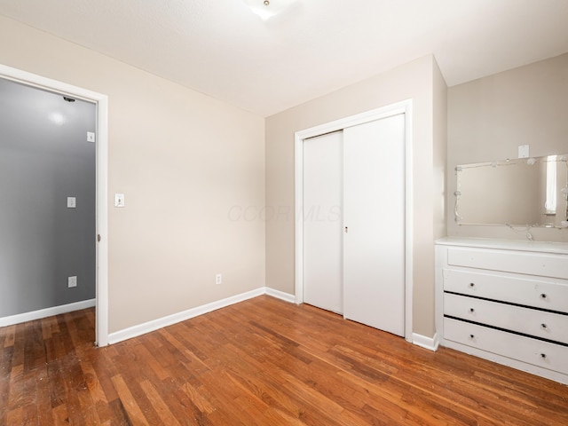 unfurnished bedroom featuring wood finished floors, baseboards, and a closet