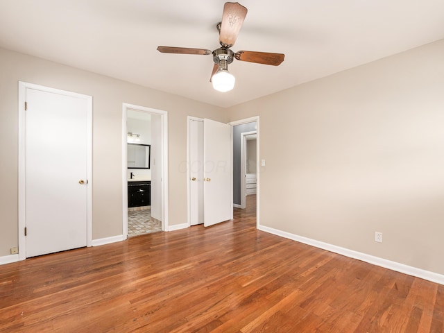 unfurnished bedroom with wood finished floors, baseboards, connected bathroom, and a ceiling fan