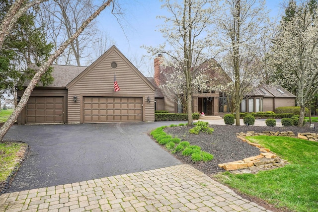 view of front facade with an attached garage, driveway, and a chimney