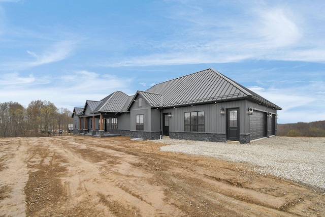rear view of house featuring board and batten siding, a standing seam roof, metal roof, an attached garage, and driveway