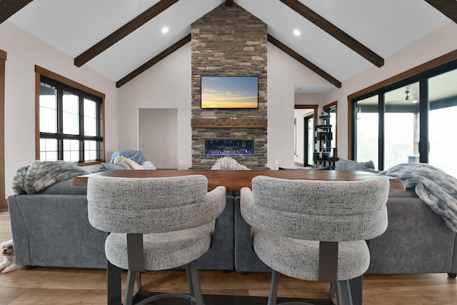 living room with a stone fireplace, beamed ceiling, a healthy amount of sunlight, high vaulted ceiling, and wood finished floors
