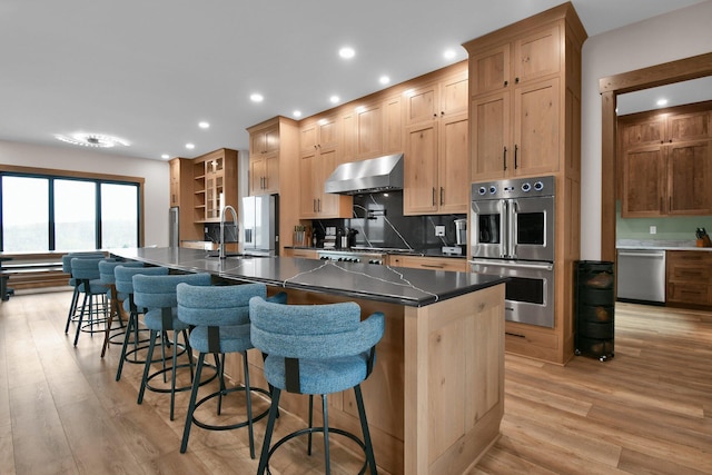 kitchen featuring wall chimney range hood, dark countertops, a sink, stainless steel appliances, and light wood finished floors