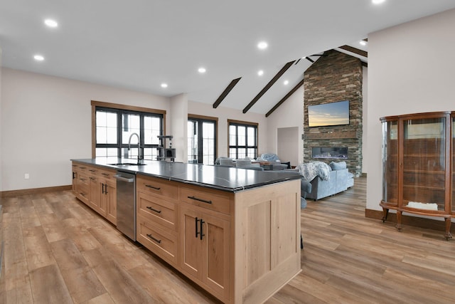kitchen with a stone fireplace, dark countertops, light wood-style floors, a sink, and light brown cabinetry