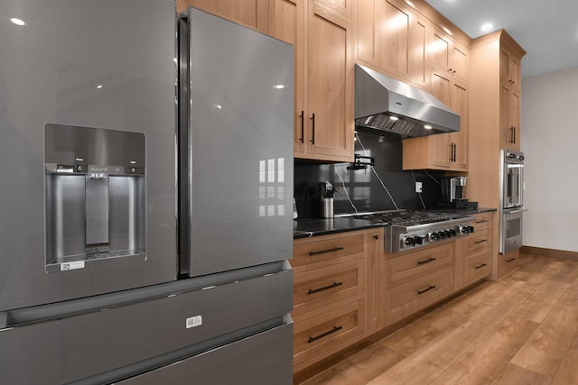 kitchen featuring wall chimney exhaust hood, decorative backsplash, dark countertops, stainless steel appliances, and light wood finished floors