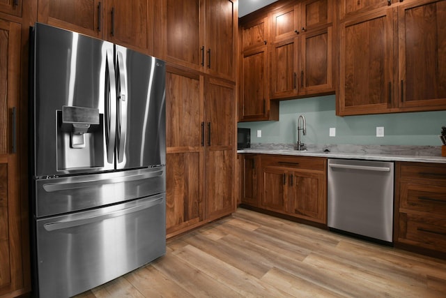 kitchen with a sink, brown cabinetry, light wood-type flooring, and stainless steel appliances