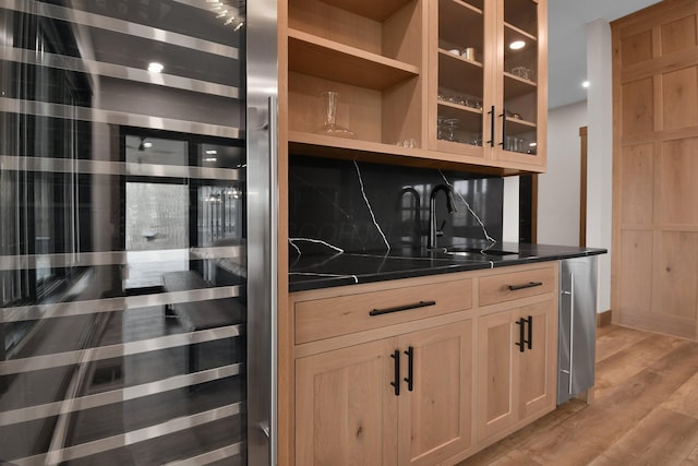 bar with light wood-type flooring, decorative backsplash, a sink, and beverage cooler
