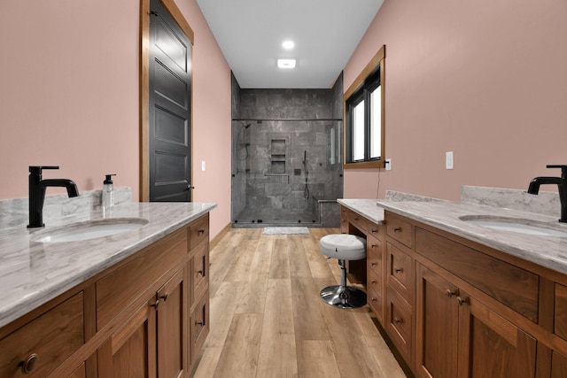 bathroom featuring a shower stall, two vanities, wood finished floors, and a sink