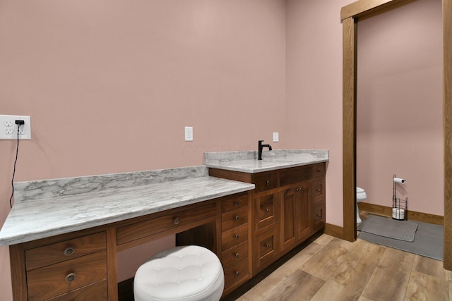 bathroom with toilet, vanity, wood finished floors, and baseboards