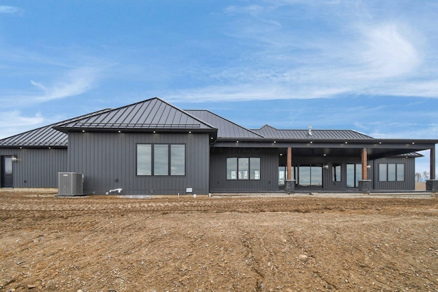 back of house with central air condition unit, a standing seam roof, and metal roof