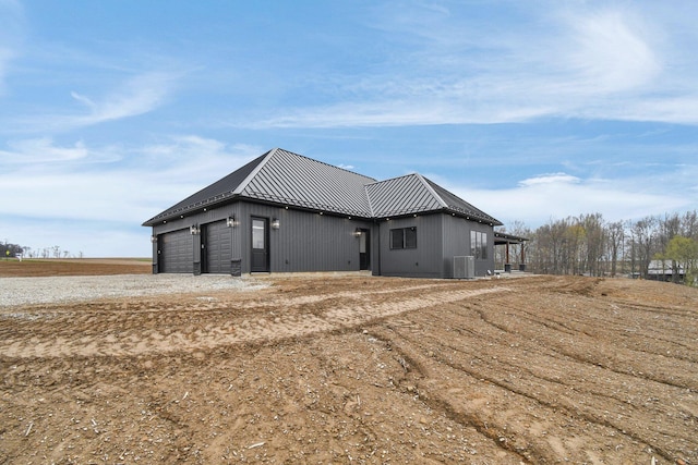view of side of home with cooling unit, metal roof, and a garage