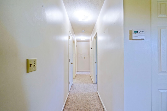 hallway featuring baseboards, light colored carpet, and a textured ceiling