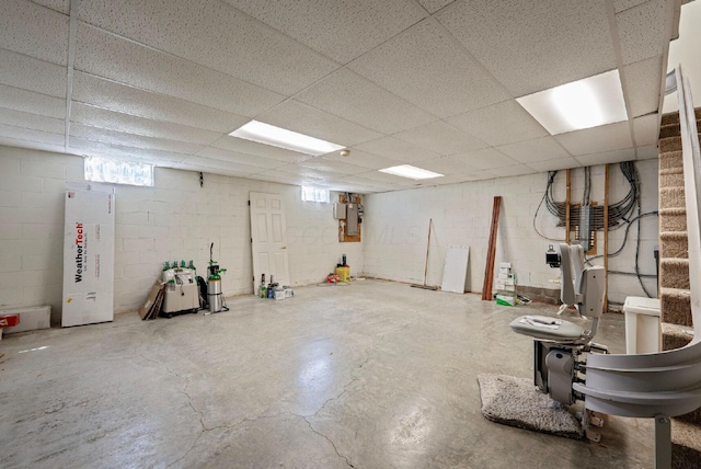 below grade area with a drop ceiling, electric panel, and concrete block wall