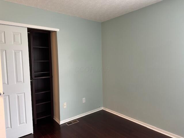unfurnished bedroom featuring dark wood-style flooring, visible vents, baseboards, and a textured ceiling