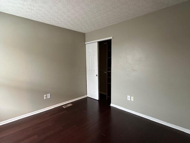 unfurnished room featuring visible vents, baseboards, wood finished floors, and a textured ceiling