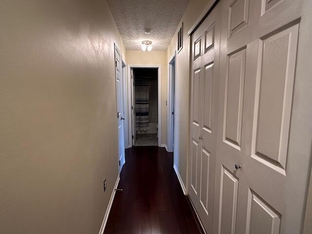 corridor with a textured ceiling, baseboards, and dark wood-style floors