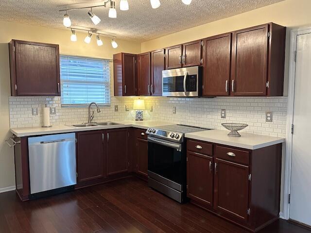kitchen with a sink, dark wood-style flooring, light countertops, stainless steel appliances, and backsplash