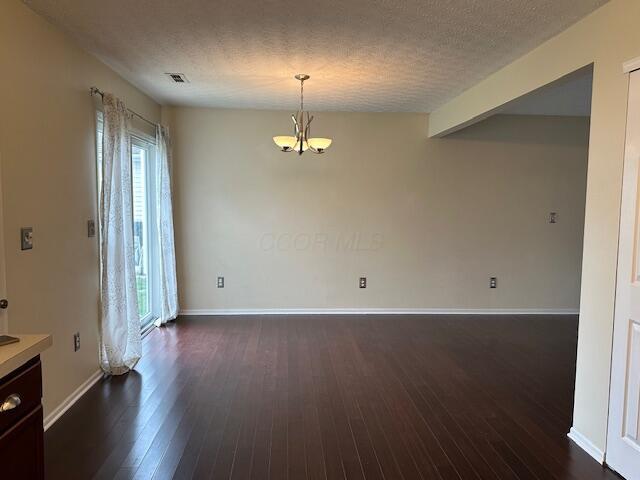 unfurnished dining area with a healthy amount of sunlight, an inviting chandelier, dark wood-style floors, and visible vents