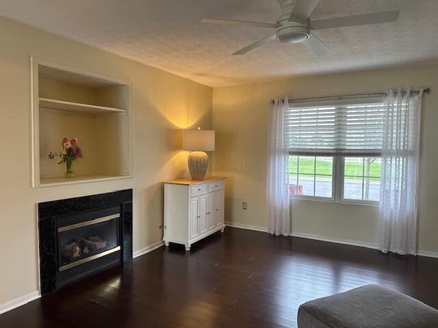 interior space featuring a textured ceiling, a ceiling fan, a glass covered fireplace, baseboards, and dark wood-style floors