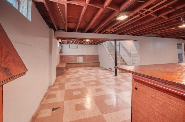 below grade area featuring stairs, concrete block wall, and light floors