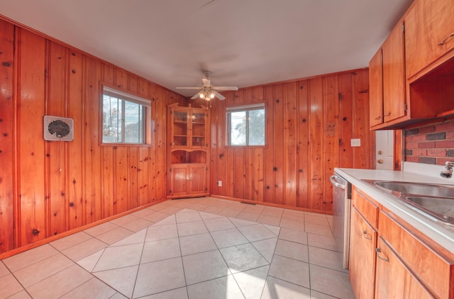 kitchen with wooden walls, light tile patterned floors, light countertops, stainless steel dishwasher, and a sink