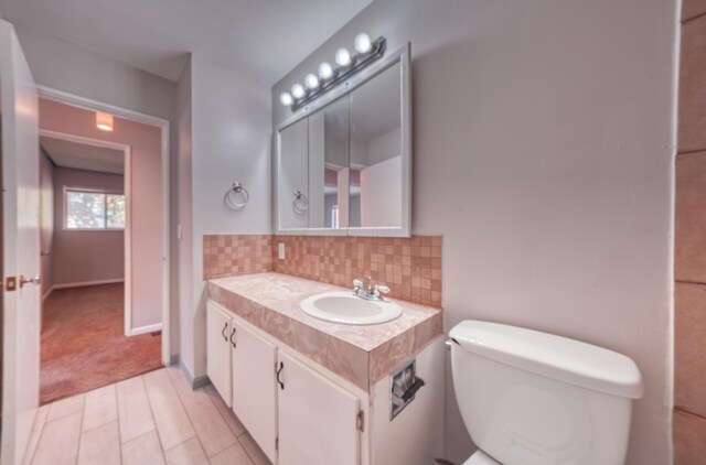 bathroom with tasteful backsplash, toilet, vanity, and baseboards