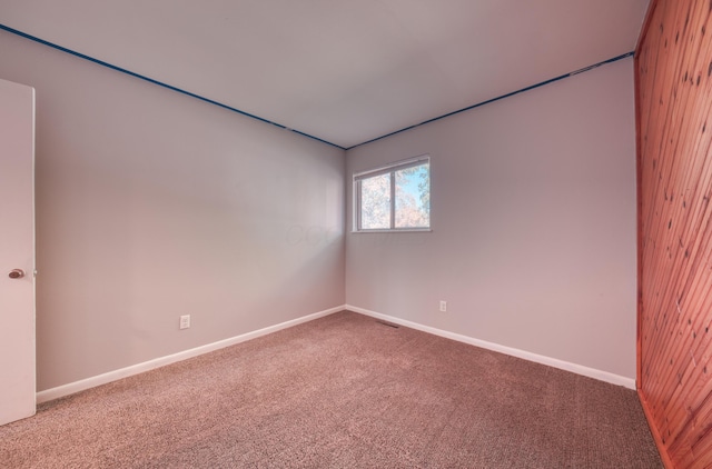 unfurnished room featuring wood walls, baseboards, visible vents, and carpet floors