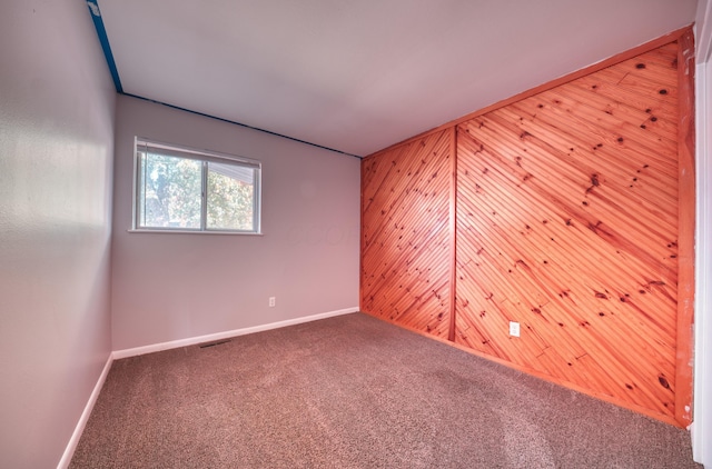 unfurnished room featuring wood walls, visible vents, baseboards, and carpet floors