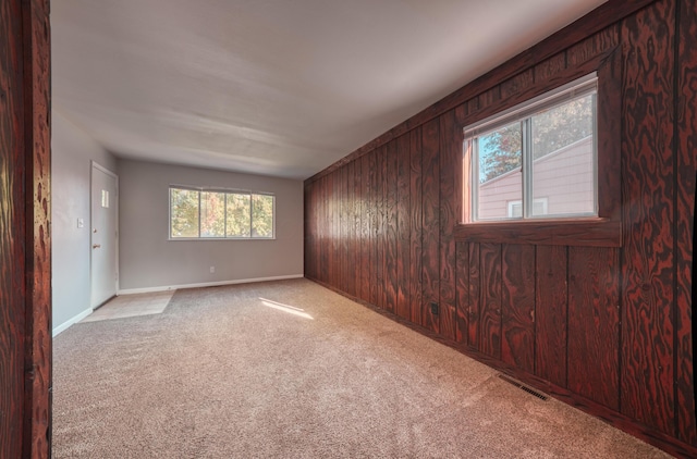 carpeted spare room with wood walls, baseboards, and visible vents
