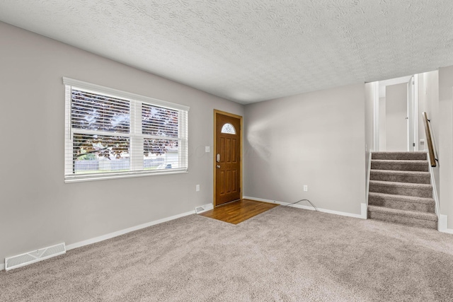 carpeted entryway with stairway, a textured ceiling, baseboards, and visible vents