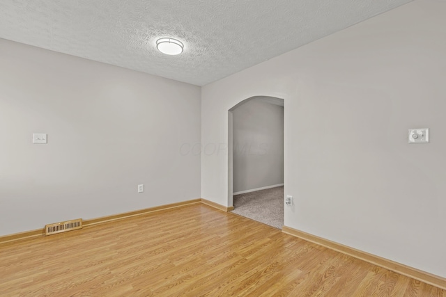 unfurnished room featuring a textured ceiling, baseboards, visible vents, wood finished floors, and arched walkways