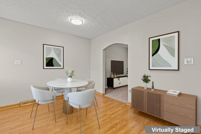 dining space featuring arched walkways, light wood-type flooring, a textured ceiling, and baseboards