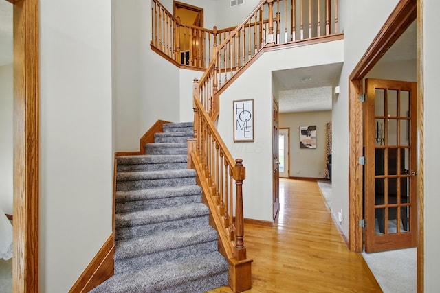 stairs with a high ceiling, wood finished floors, baseboards, and visible vents