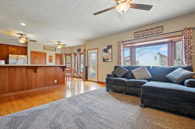 living room featuring ceiling fan, light wood-type flooring, baseboards, and a textured ceiling