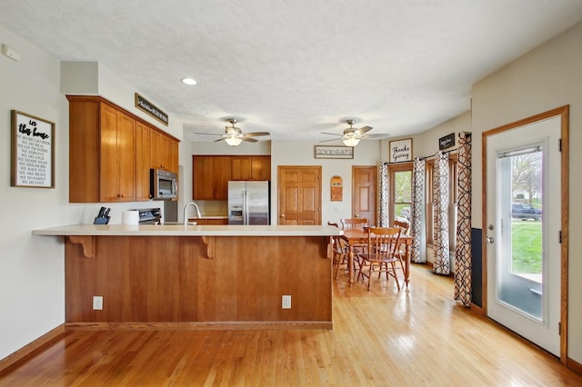 kitchen with light wood-style flooring, a peninsula, light countertops, stainless steel appliances, and brown cabinets