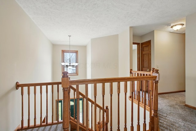 corridor featuring an inviting chandelier, a textured ceiling, carpet floors, an upstairs landing, and baseboards