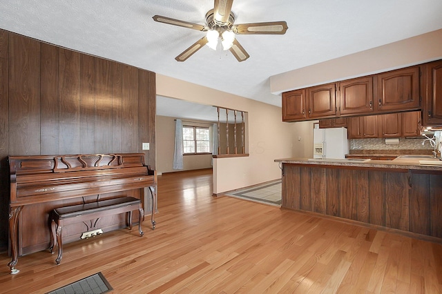 kitchen with ceiling fan, a peninsula, light wood-style floors, backsplash, and white refrigerator with ice dispenser
