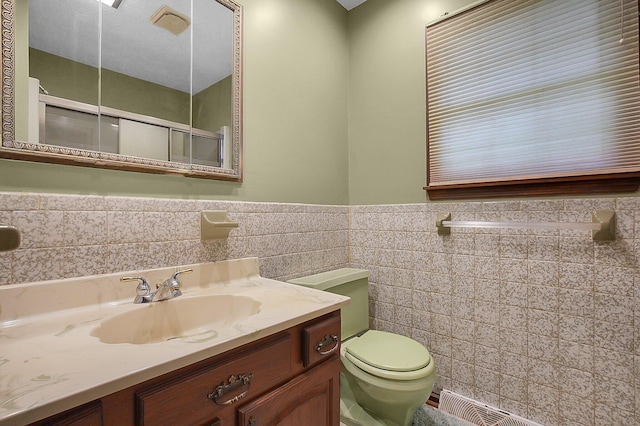 full bath with vanity, toilet, a wainscoted wall, a shower with shower door, and tile walls
